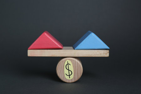 gender pay gap. Wooden triangles as male and female symbols on miniature seesaw against black backgroundの写真素材