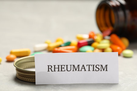 Card with word Rheumatism and pills on light tableの写真素材