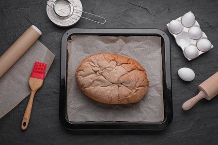 Baking pan with bread, parchment paper and ingredients on black slate background, flat lay