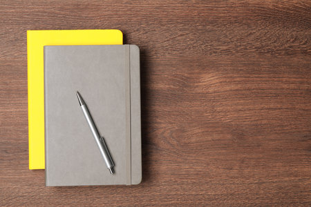 Stylish notebooks and pen on wooden table, top view. Space for text