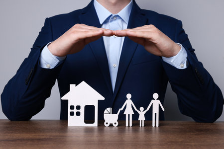 Man protecting figures of family and house at wooden table. closeup. insurance concept