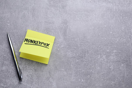 Paper note with word Monkeypox and pen on light gray table, flat lay. Space for text