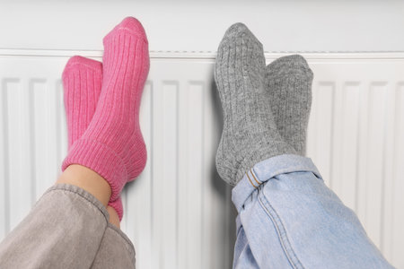 People warming feet near heating radiator, closeup