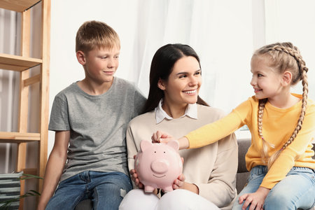 Happy family putting coin into piggy bank at homeの写真素材