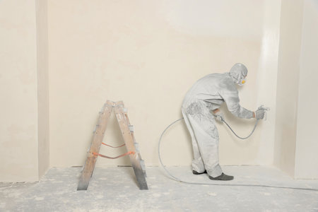 Decorator in protective overalls painting wall with spray gun indoorsの写真素材