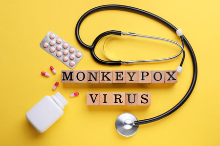 Words Monkeypox Virus made of wooden cubes, pills and stethoscope on yellow background, flat layの写真素材