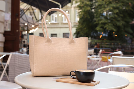 Stylish bag and cup of coffee on white table in outdoor cafeの写真素材