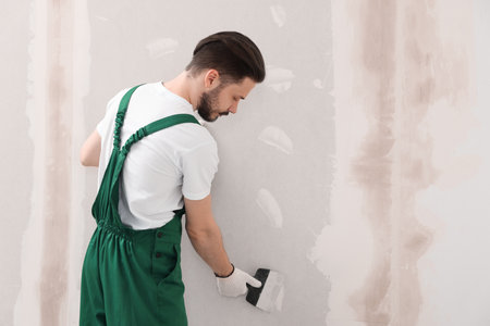 Worker in uniform plastering wall with putty knife indoors. Space for textの写真素材