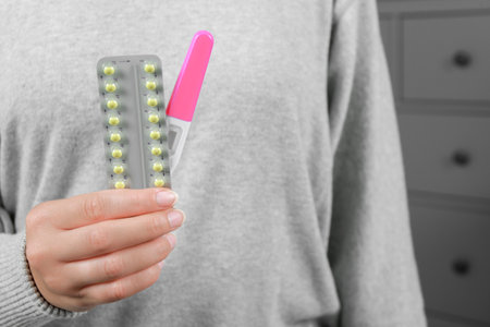 Woman holding birth control pills and pregnancy test indoors, closeupの写真素材