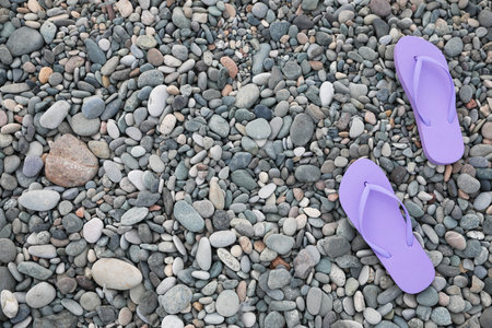 Stylish violet flip flops on pebble seashore, top view. Space for textの写真素材