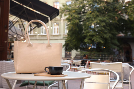 Stylish bag and cup of coffee on white table in outdoor cafe, space for textの写真素材