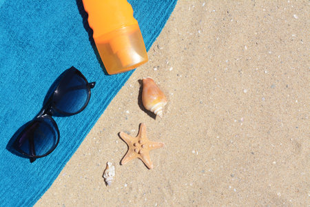 Stylish sunglasses, bottle of sunblock and blue towel on sand, flat lay with space for text. beach accessoriesの写真素材