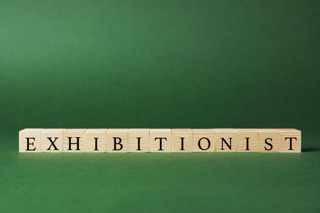Word EXHIBITIONIST made with wooden cubes on dark green background