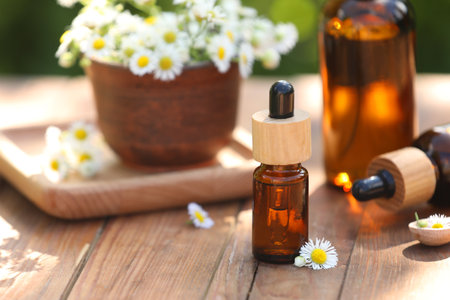 Bottles of chamomile essential oil and flowers on wooden table, closeup. Space for textの写真素材