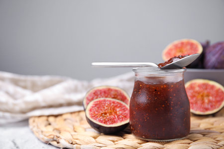 Glass jar of tasty sweet fig jam with spoon and fruits on table. Space for textの写真素材