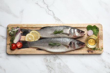 Tasty sea bass fish and ingredients on white marble table, top viewの写真素材