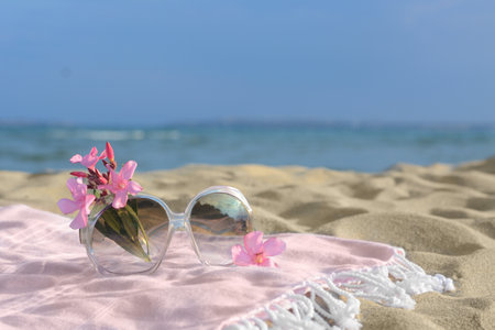 Beautiful sunglasses with tropical flower on blanket near the sea. Space for textの写真素材
