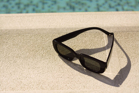 Stylish sunglasses near outdoor swimming pool on sunny day, space for textの写真素材