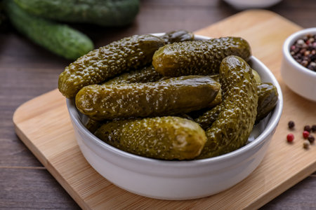 Bowl of pickled cucumbers and ingredients for food preservation on wooden table, closeup