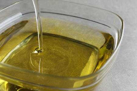 Pouring cooking oil into bowl on light background, closeupの写真素材