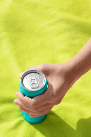 Woman holding aluminum can with beverage on yellow blanket, closeup
