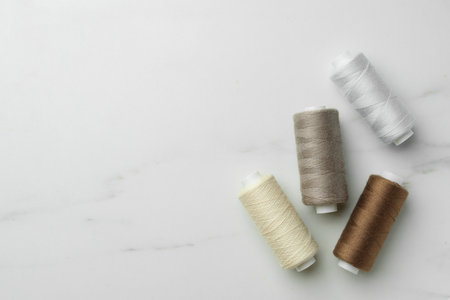 Sewing threads on white marble table, flat lay. Space for text