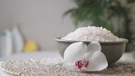 Bowl with bath salt and flower on wicker mat indoors, space for textの写真素材