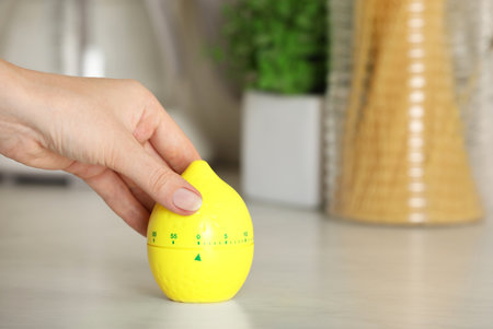 Woman winding up kitchen timer in shape of lemon at white table indoors, closeup. Space for textの写真素材