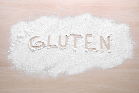 Word Gluten written with flour on wooden table, top viewの写真素材