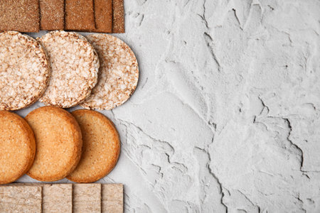 Rye crispbreads, rice cakes and rusks on white textured table, flat lay. Space for text