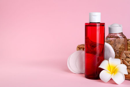 Bottles of micellar water, plumeria flower and cotton pads on pink background. Space for textの写真素材