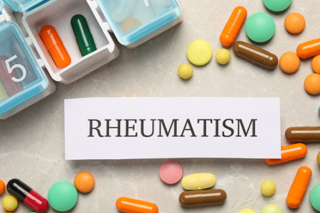 Card with word Rheumatism and pills on light marble table, flat layの写真素材