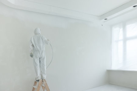Decorator painting wall on ladder near windows in room, back viewの写真素材