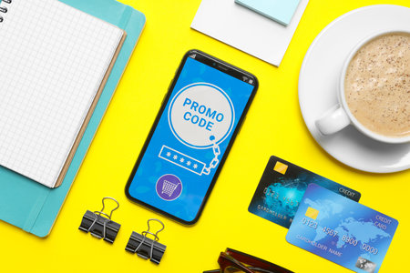Flat lay composition of smartphone with activated promo code, credit cards and stationery on yellow tableの写真素材