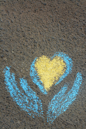 Heart with hand drawn with blue and yellow chalks on asphalt outdoors, top viewの写真素材