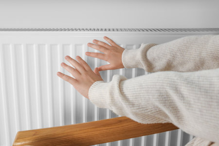 Little girl warming hands near heating radiator indoors, closeupの写真素材