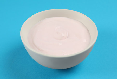 Bowl of tasty organic yogurt on light blue backgroundの写真素材