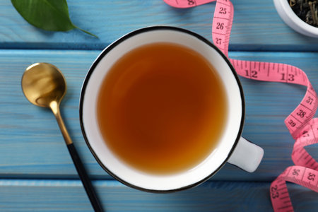 Cup of herbal diet tea and measuring tape on light blue wooden table, flat lay. weight loss conceptの写真素材