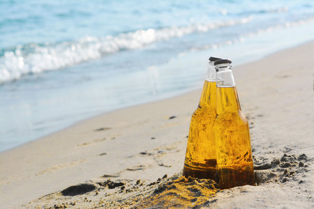 Bottles of cold beer on sandy beach near sea, space for textの写真素材