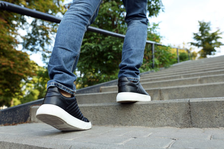 Man in stylish black sneakers walking up stairs, closeup