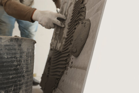 Worker applying cement on wall tile for installation indoors, closeupの写真素材