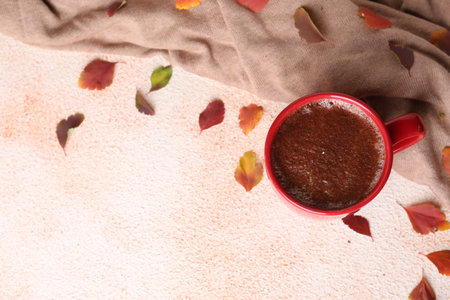 Cup of hot drink, leaves and soft knitted fabric on beige textured table, flat lay with space for...