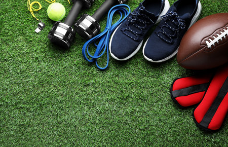 Set of different colorful sports equipment on green grass, flat lay. Space for text