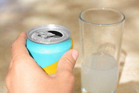 Woman holding aluminum can with drink on blurred background, closeup