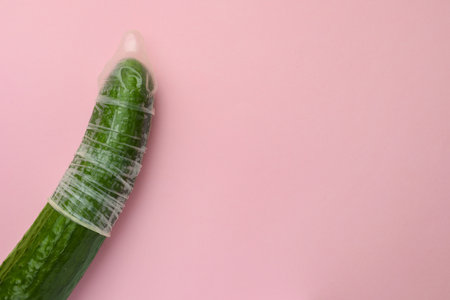 Cucumber with condom on pink background, top view and space for text. Safe sex conceptの写真素材