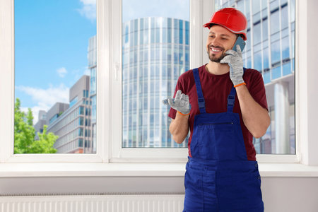 Professional repairman in uniform talking on phone indoors, space for text