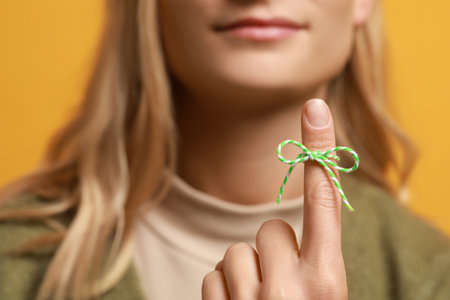 Woman showing index finger with tied bow as reminder against orange background, focus on hand