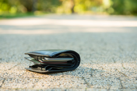 Black lost wallet lying on ground outdoors, closeup. Space for text