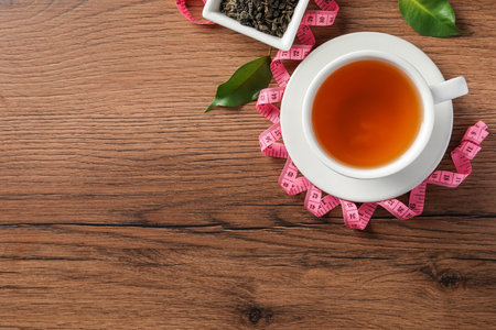 Cup of herbal diet tea and measuring tape on wooden table, flat lay with space for text. weight loss conceptの写真素材