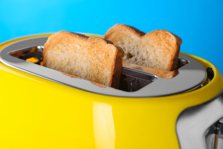 Modern toaster with slices of roasted bread against light blue background, closeupの写真素材